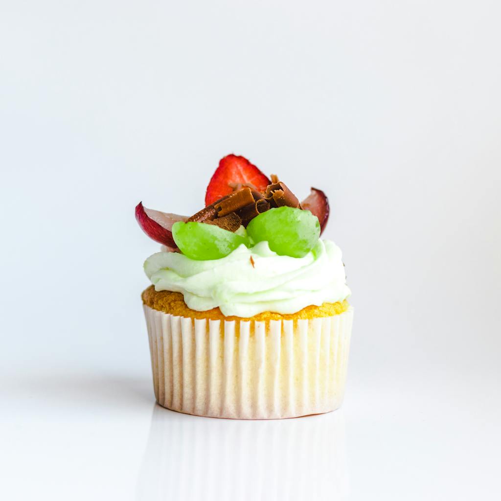 Close-up of a cupcake topped with strawberries, grapes, and chocolate curls, perfect for dessert lovers.