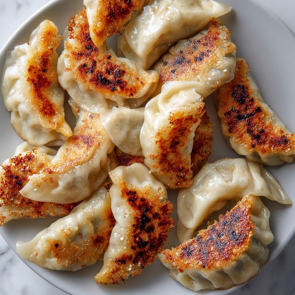 The image shows several dumplings arranged closely together on a white plate atop a white marbled surface. Each dumpling has a soft, pale dough exterior with pleated edges, and most have a golden-brown crispy bottom that contrasts with the slightly translucent, smooth dough on top. The dumplings vary slightly in shape and size, and the browned parts have a textured, slightly crunchy look, while the upper part retains a soft, tender appearance. photo taken with an iphone --ar 4:5 --v 7