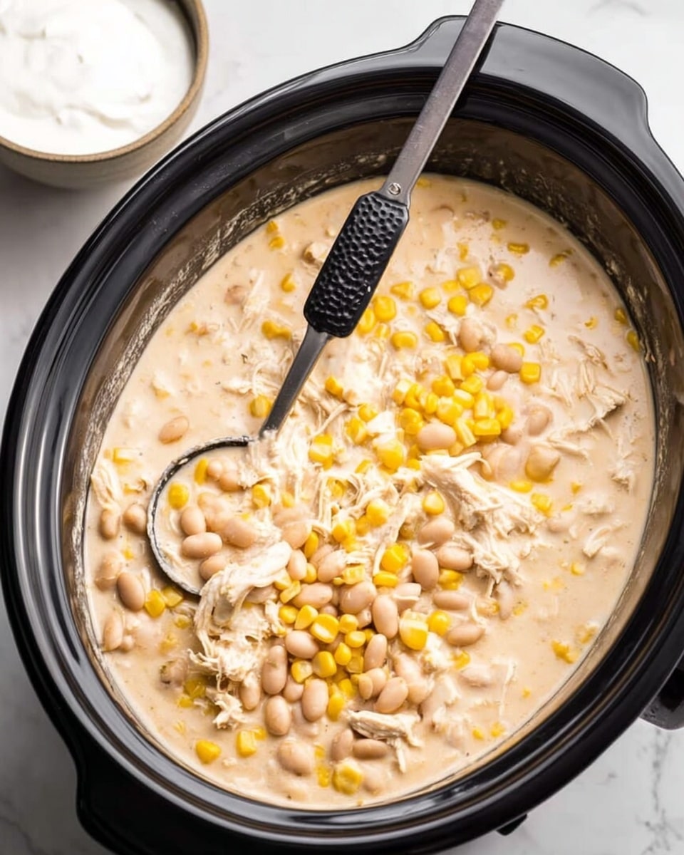 A white bowl filled with creamy white chicken soup containing three visible layers: the base layer is a smooth, light beige broth mixed with white beans and corn; the middle layer has shredded white chicken pieces scattered evenly; the top layer features thin orange crispy strips placed in the center, garnished with finely chopped green herbs, a dollop of white sour cream on one side, and two bright green lime wedges on the other side. Around the bowl, there are loose lime wedges, orange crispy strips, a small white bowl of sour cream, a clear bowl filled with crispy strips, and a blue and white checkered cloth, all set on a white marbled surface. photo taken with an iphone --ar 4:5 --v 7