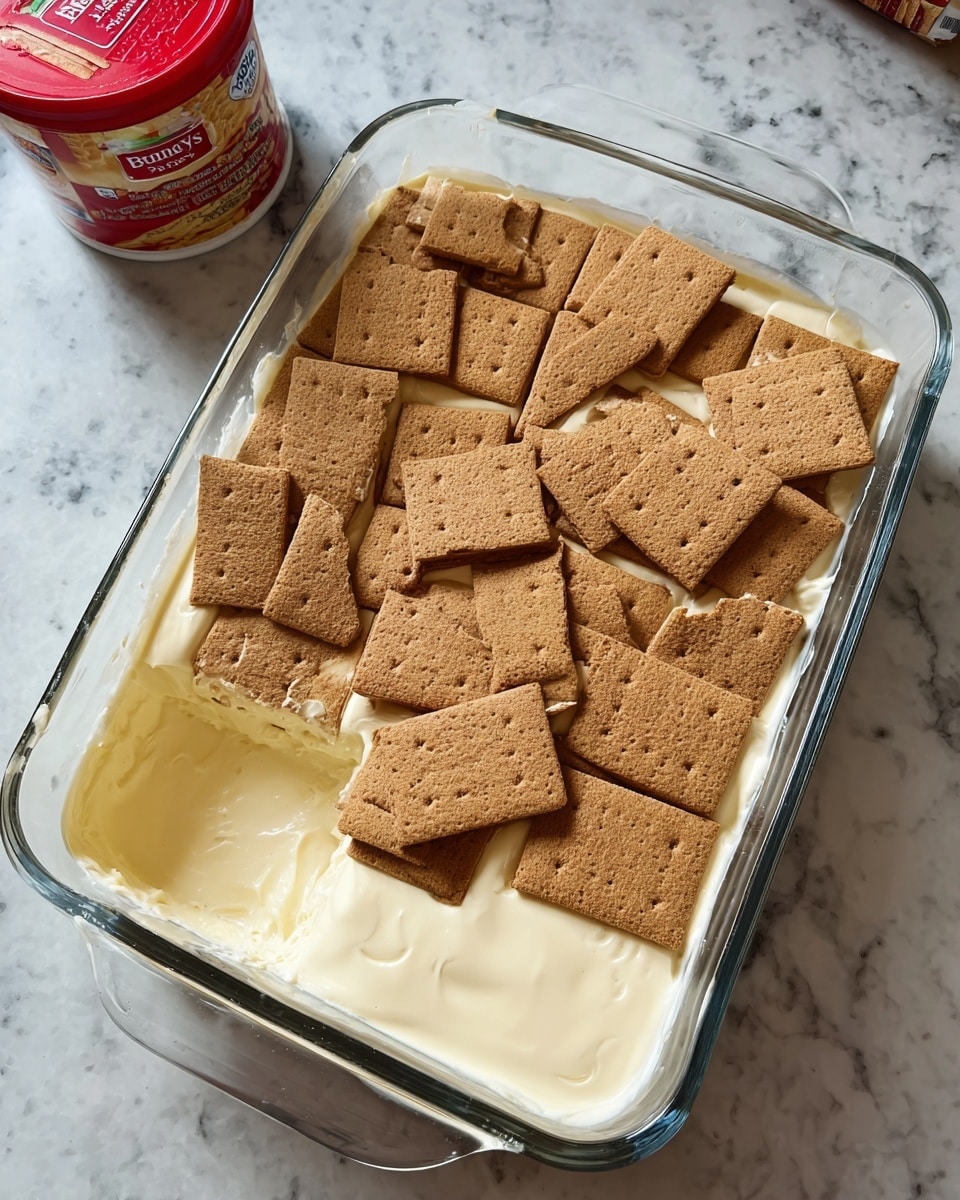 The image shows a glass baking dish with a layered dessert that has been partially eaten from one corner. The bottom layer consists of light brown crust or biscuit crumbs with a crumbly texture. Above that is a thick creamy layer in pale cream color, smooth and soft. The topmost layer is a shiny, thick chocolate coating with a rich dark brown color that looks glossy and slightly wavy, partly pulled back revealing the layers underneath. The dish is placed on a white marbled surface. Photo taken with an iphone --ar 4:5 --v 7