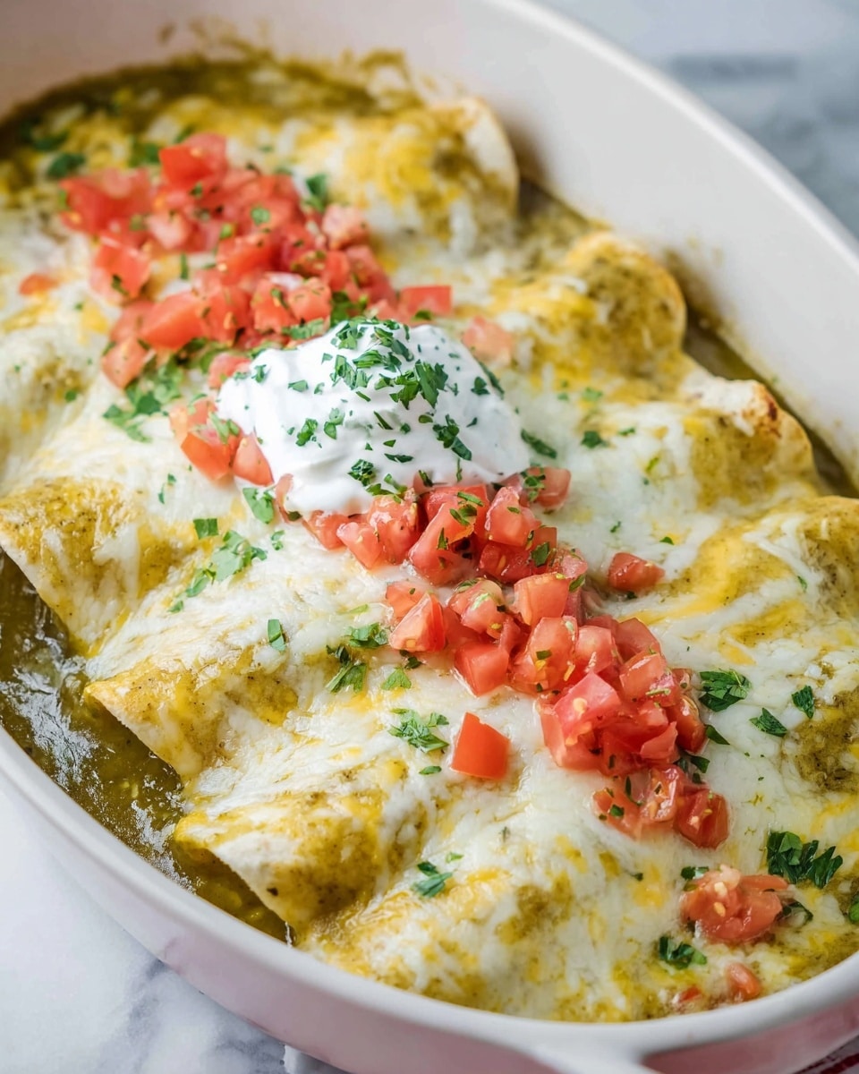 A white oval dish filled with three rolled enchiladas covered in creamy melted white cheese mixed with light yellow melted cheese. The enchiladas sit in a green sauce that pools slightly around their edges. On top, there is a line of chopped fresh red tomatoes and scattered green chopped herbs. A dollop of white sour cream sprinkled with herbs is placed near the center. The dish rests on a white marbled surface. photo taken with an iphone --ar 4:5 --v 7