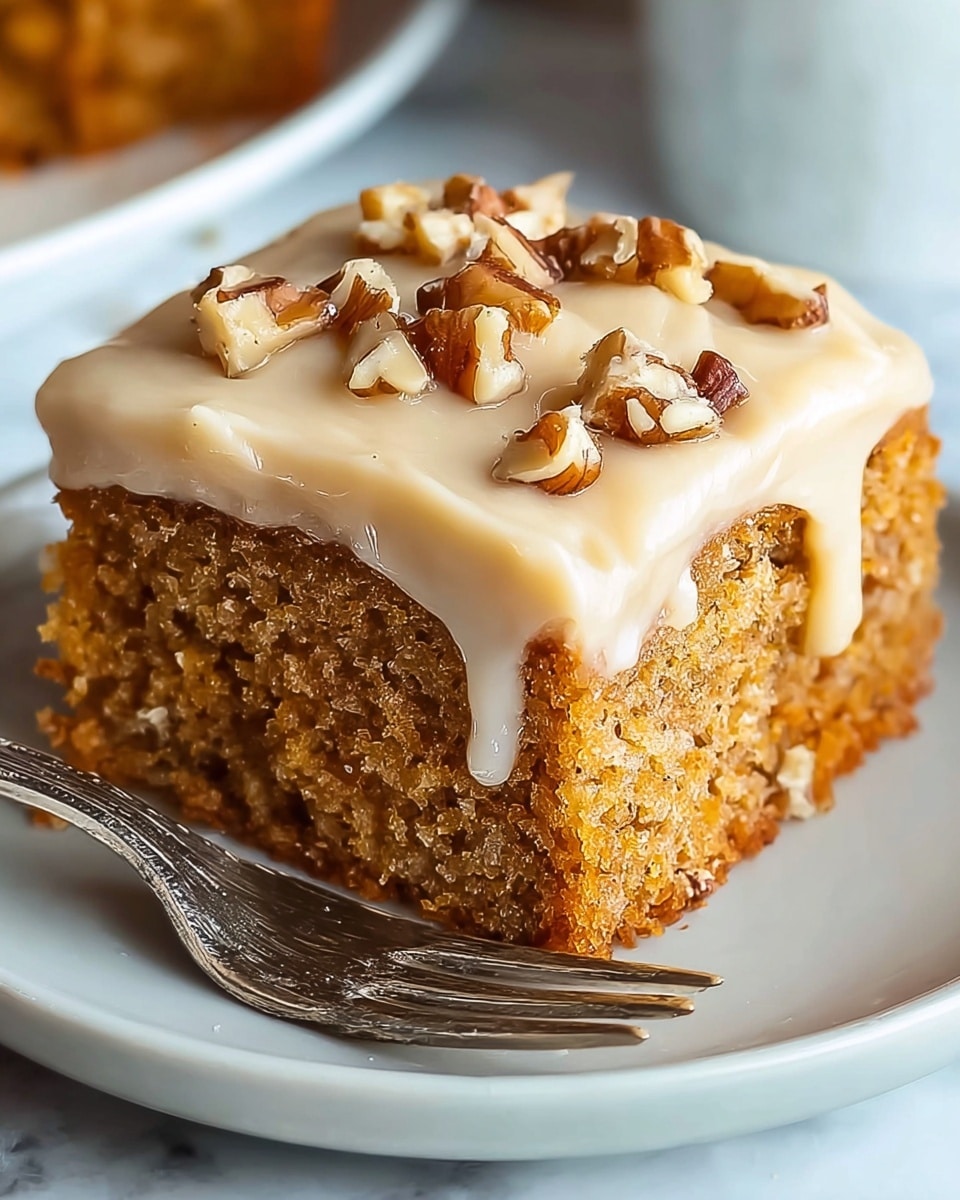 A close-up of a single square piece of moist, brown cake with a dense, crumbly texture. It has a thick, smooth layer of creamy white frosting spread evenly on top, with several chopped walnuts scattered in a small pile at the center. The cake sits on a white plate with a silver fork placed beside it, all set on a white marbled surface. The photo taken with an iphone --ar 4:5 --v 7