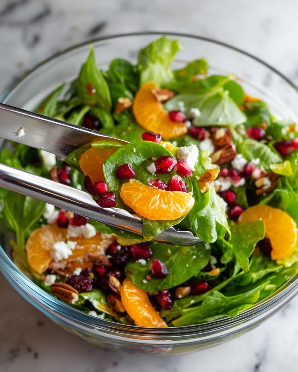 A clear glass bowl holds a fresh salad with a mix of leafy greens including spinach and darker red lettuce as the base layer. On top, bright orange mandarin slices are scattered evenly, contrasted by popping red pomegranate seeds spread across the salad. Small chunks of white feta cheese are sprinkled generously, adding texture and color, while chopped brown pecans are mixed in for crunchy bits. The bowl sits on a white marbled surface, creating a clean and bright background with a whole orange and green leaves blurred softly in the back. photo taken with an iphone --ar 4:5 --v 7
