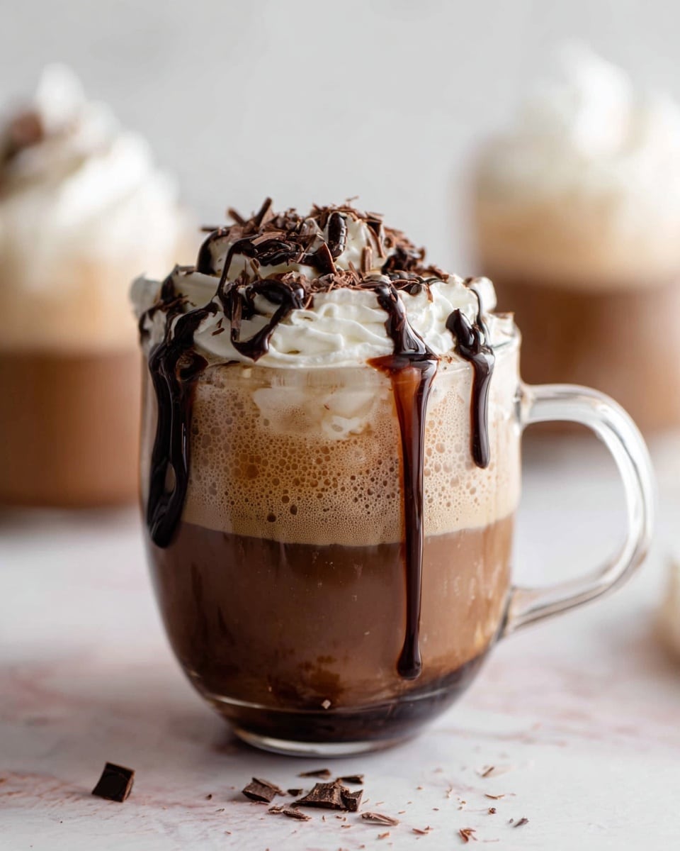 A clear glass cup filled with dark black coffee is shown with creamy white milk being poured from a clear glass pitcher above, creating a swirling mix where the two liquids meet. The cup is resting on a white marbled surface with a soft pink cloth to the left. In the blurry background, there is another glass cup topped with whipped cream and some chocolate shavings on top. photo taken with an iphone --ar 4:5 --v 7
