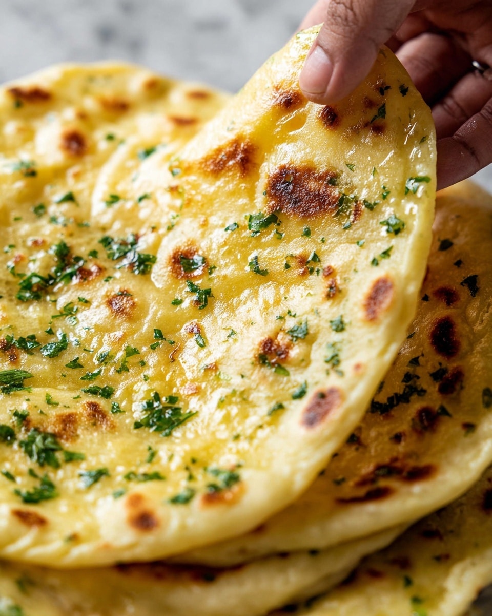 The image shows a stack of flatbreads with golden brown spots on a white plate. Each flatbread is thin, soft, and slightly bubbly with a light golden color. The top layer is covered with melted butter and finely chopped green herbs evenly spread across the surface, giving it a fresh and vibrant look. The flatbreads are layered on top of each other, showing some overlapping edges, and there is a wooden bowl with coarse salt on the right side of the plate. The background is a white marbled texture. photo taken with an iphone --ar 4:5 --v 7
