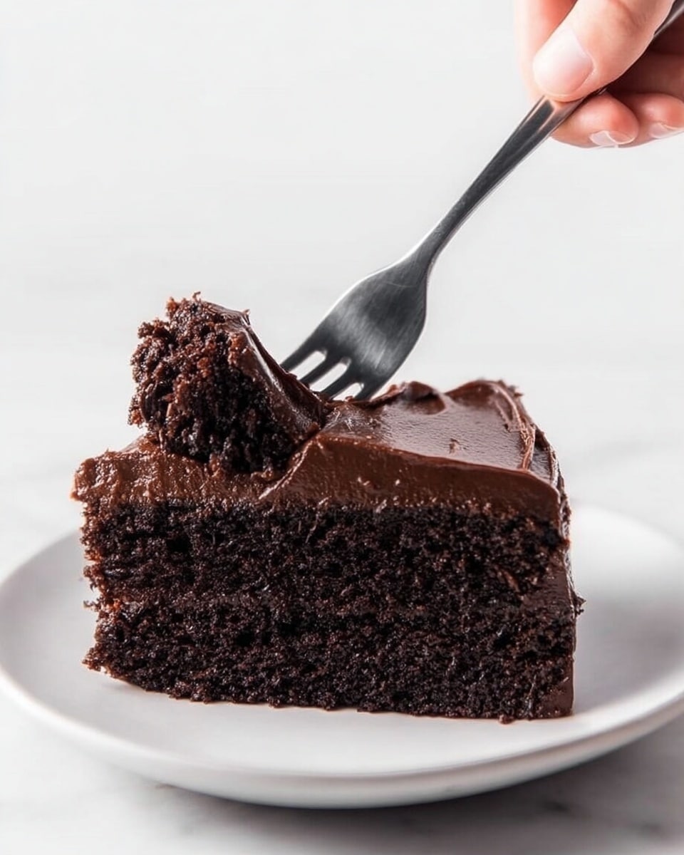 A single slice of dark chocolate cake sits on a white plate against a white marbled texture. The cake has one thick bottom layer that looks moist and soft, with a rich dark brown color. On top, there is one thick layer of glossy chocolate frosting, smooth but slightly textured from spreading. A woman's hand is holding a fork that has taken a bite from the front left side of the cake, lifting a piece covered in chocolate frosting. Photo taken with an iphone --ar 4:5 --v 7