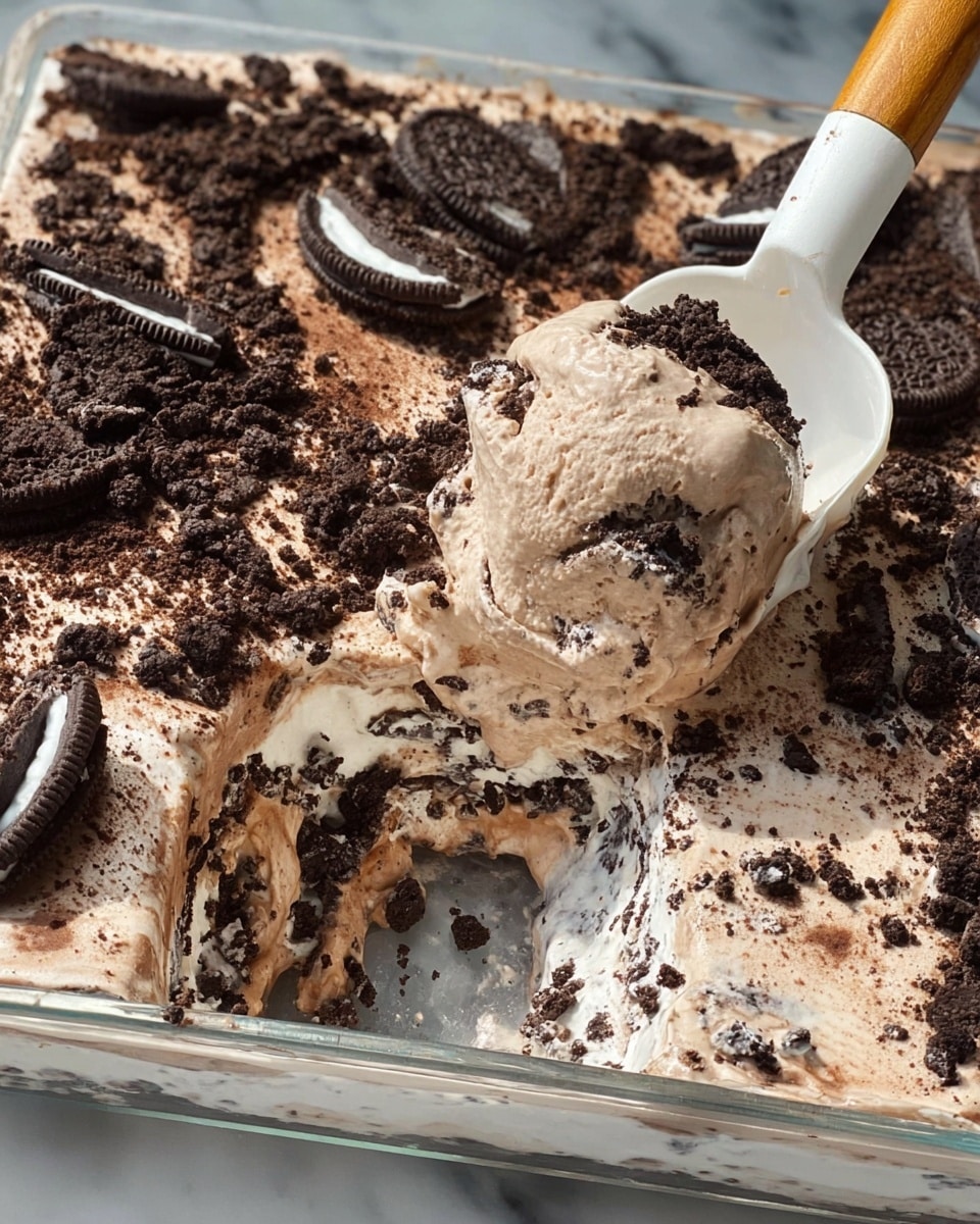 A dish in a clear rectangular glass container shows three visible layers, with a white spatula scooping some of it. The bottom layer is a thin, darker brown chocolate crust. Above it is a thick cream-colored layer with small black cookie pieces embedded inside. The top layer is a light, fluffy chocolate mousse mixed with large chunks of dark chocolate sandwich cookies scattered across the surface. The mousse appears smooth with some texture from the cookie bits. The scene is set against a white marbled texture background. photo taken with an iphone --ar 4:5 --v 7