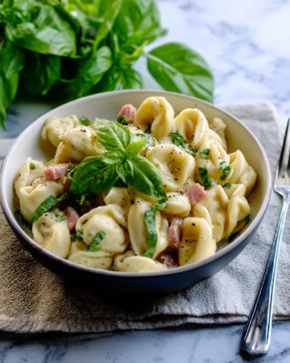 A white bowl filled with tortellini pasta coated in a creamy sauce with small pieces of crispy bacon scattered on top. The pasta is light yellow with delicate folds, and the sauce has a smooth, slightly glossy texture. Beside the bowl, there is a clear glass of sparkling wine, and the background features a white marbled surface. The scene is bright and clean, emphasizing the warm colors of the dish. Photo taken with an iphone --ar 4:5 --v 7