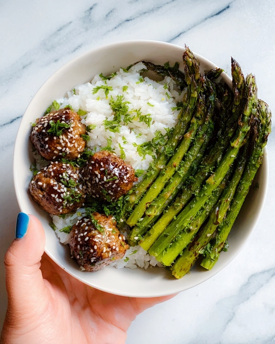 A white bowl filled with three layers: on the left side, several brown glazed meatballs sprinkled with sesame seeds and small green pieces of chopped herbs; in the center and under the meatballs, a layer of fluffy white rice; and on the right side, a bunch of green grilled asparagus with grill marks, slightly shiny from oil. A woman's hand with blue nail polish holds the edge of the bowl, resting on a white marbled surface. Photo taken with an iphone --ar 4:5 --v 7