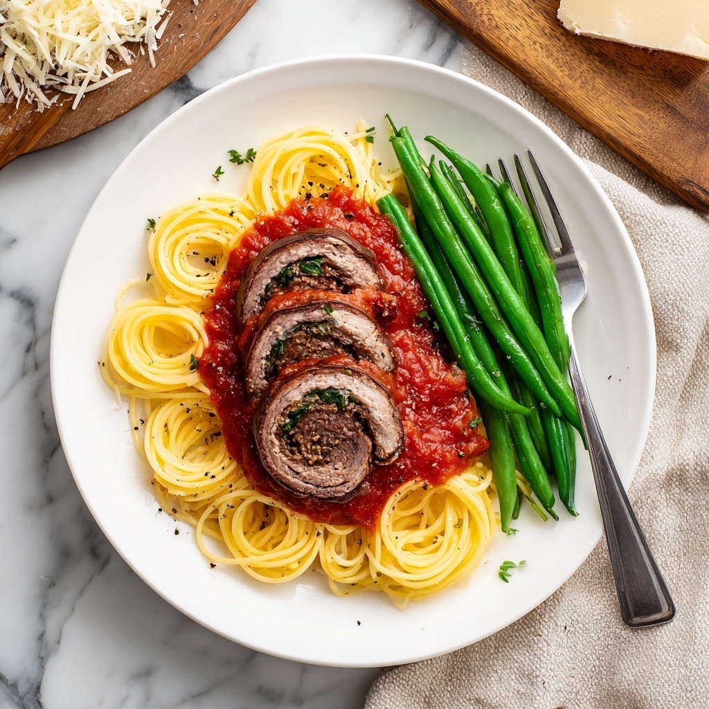 A white plate holds a meal with three main layers. The bottom layer is light yellow spaghetti, loosely arranged in a circular shape. On top of the spaghetti lies a bright red tomato sauce, spread unevenly with some chunks visible. On the sauce are two thick slices of stuffed beef roll, showing a dark brown outer edge and a mixed brown and green filling inside. To the right side of the plate, bright green steamed green beans are laid next to the spaghetti, sprinkled lightly with black pepper. A silver fork rests on the right edge of the plate. The background is a white marbled texture with parts of a beige cloth and a wooden cutting board containing grated cheese seen in the scene. photo taken with an iphone --ar 4:5 --v 7