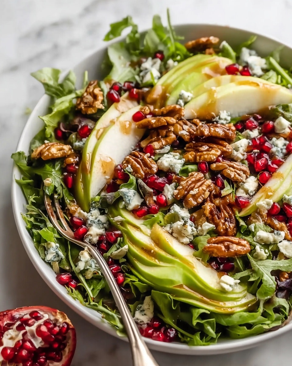 A large white bowl on a white marbled surface holds a fresh salad with multiple layers: the bottom layer is made of mixed green leafy lettuce with a slightly ruffled texture, topped with sliced green avocado and pear pieces showing smooth light green and creamy white flesh. Scattered among these are bright red pomegranate seeds adding a jewel-like touch, along with crumbled blue cheese providing small white chunks with blue veins. Whole glazed walnuts with a shiny brown texture are placed on top, and a silver fork rests inside the bowl. Photo taken with an iphone --ar 4:5 --v 7