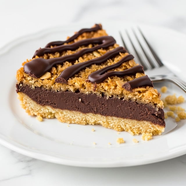 A close-up view of a triangular slice of dessert bar on a white plate with a white marbled surface underneath. The bottom layer is a light golden crumbly crust. Above it is a thick dark chocolate layer, smooth and glossy. The top layer is a golden, sticky mixture with visible oatmeal or coconut flakes, giving a rough texture. Dark chocolate is drizzled unevenly across the top in broad, wavy lines. Some crumbs are scattered near the slice on the plate, and a silver fork is placed to the right side. Photo taken with an iphone --ar 4:5 --v 7