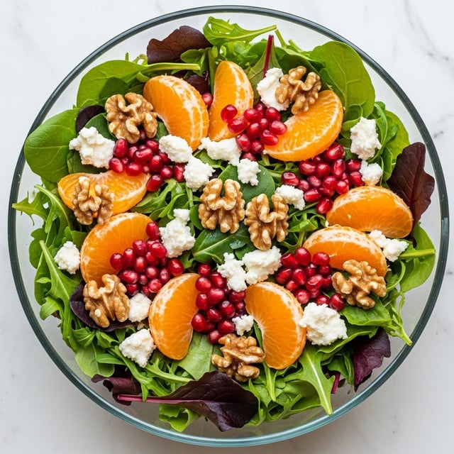 A fresh salad in a clear glass bowl sits on a white marbled surface, showing several layers and colors. The bottom layer is mixed green leaves with some darker purple leaves, providing a textured, leafy base. On top, there are bright orange tangerine slices arranged around the bowl, adding vibrant color and a smooth texture. Scattered among the tangerines are small clusters of red pomegranate seeds, giving a jewel-like shine. There are also several brown, crunchy-looking walnuts spread evenly across the salad. Finally, soft white crumbles of cheese are sprinkled over everything, creating a light accent on the colorful ingredients. Photo taken with an iphone --ar 4:5 --v 7