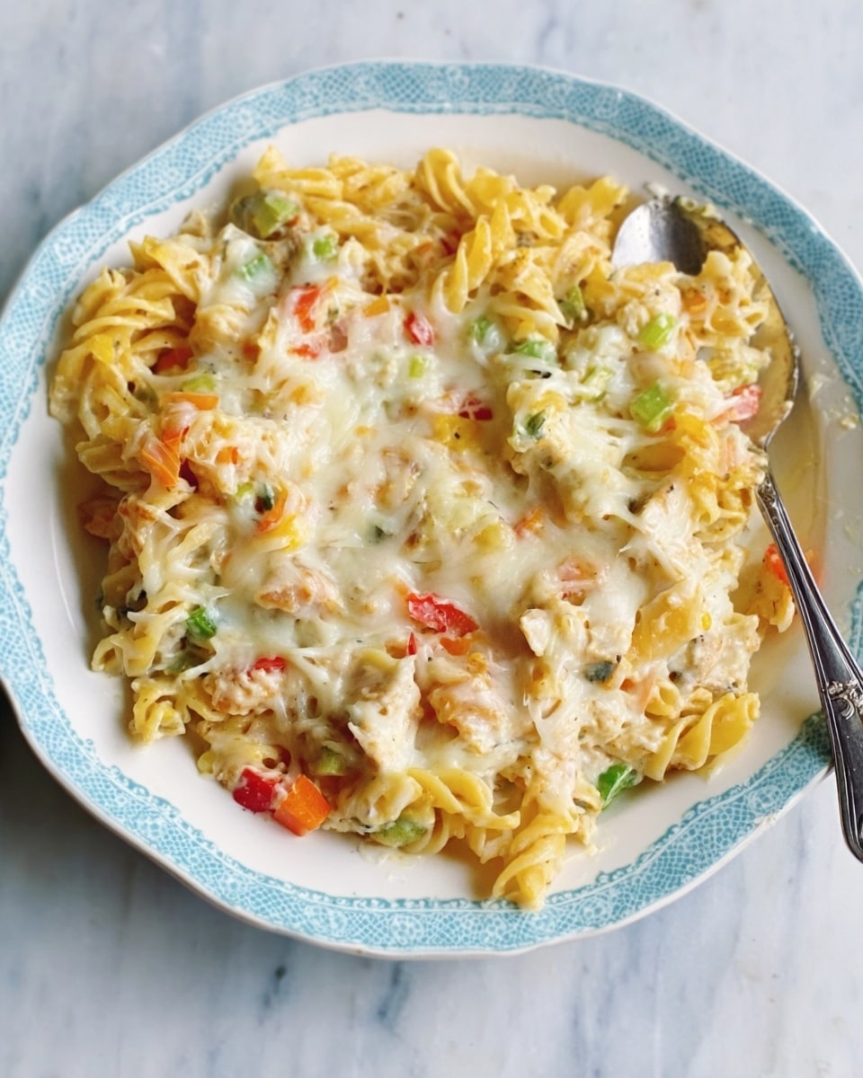 The image shows a pale blue casserole dish filled with creamy chicken and vegetable pasta. The dish has several visible layers: at the bottom is a soft layer of cooked pasta shells mixed with diced carrots and green peas, covered by a thick, white, creamy sauce mixed with chunks of chicken and scattered vegetables, giving the dish a rich and smooth texture. A silver spoon held by a woman's hand is lifting a scoop of the pasta, showing the saucy, cheesy surface on top and the mixed ingredients underneath. The background features a white marbled surface, adding a clean and bright look to the setting. Photo taken with an iphone --ar 4:5 --v 7