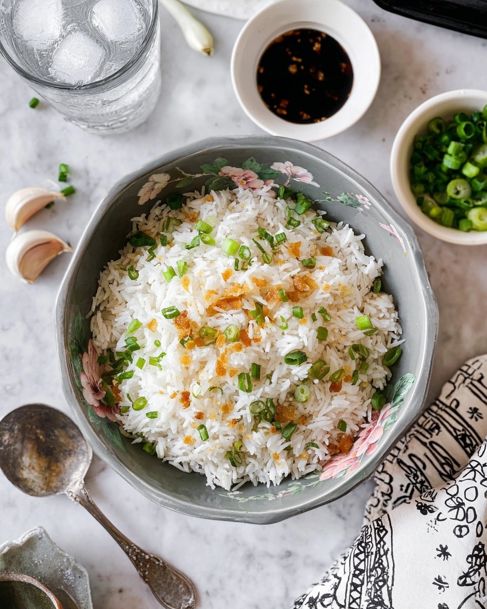 A bowl filled with white cooked rice topped with small green chopped scallions and thin golden-brown garlic slices, showing two distinct layers of white rice and scattered green and golden pieces mixed in. The bowl has a speckled gray and off-white inner surface with flower patterns near the edge. Around the bowl on a white marbled surface are small dishes of soy sauce and extra chopped scallions, a black striped cloth with garlic cloves, a silver spoon, and a clear glass of water. photo taken with an iphone --ar 4:5 --v 7