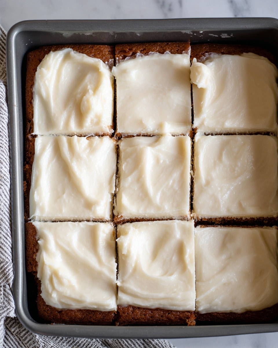 This image shows a close-up of a square piece of moist cake in a metal baking pan. The cake has two layers: the bottom layer is light brown and soft with a slightly wet, spongy texture, and the top layer is a thick, smooth, white frosting spread evenly across the cake. The cake is cut into squares, with one piece removed, revealing the inside texture and moistness of the cake's crumb. The background is a white marbled surface. photo taken with an iphone --ar 4:5 --v 7