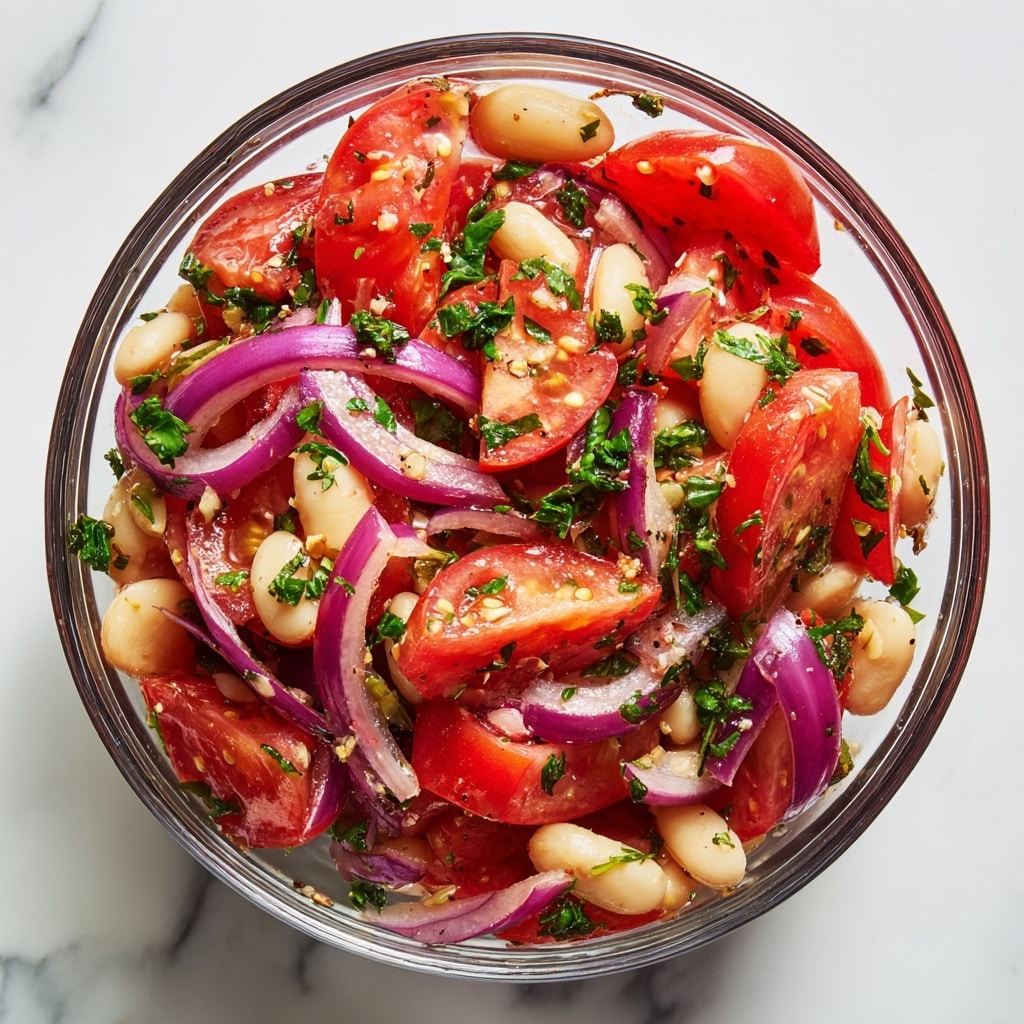 A white bowl filled with a fresh salad made of three main layers: large tomato wedges in bright red, thin slices of purple-red onion scattered throughout, and small white beans spread evenly. Green parsley leaves and chopped herbs are mixed in and sprinkled on top, adding bursts of green color. The salad is lightly dusted with a dark spice or seasoning, giving some texture on top. In the corner, there is a small white bowl with a blue floral pattern on the rim, filled with the same dark spice. The setting is on a white marbled textured surface. photo taken with an iphone --ar 4:5 --v 7