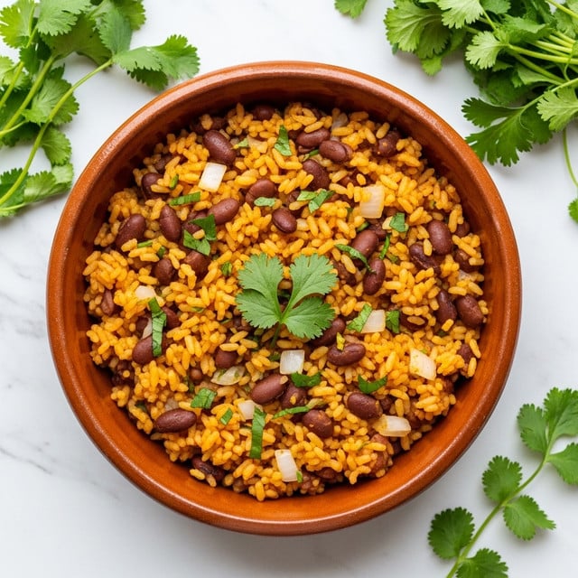 A round terracotta bowl filled with a single layer of cooked yellow-orange rice mixed with dark brown beans, small bits of white onion, and finely chopped green herbs scattered throughout. A sprig of fresh green cilantro rests on top in the center. The bowl is placed on a white marbled surface with fresh green cilantro sprigs arranged around it in the background. Photo taken with an iphone --ar 4:5 --v 7