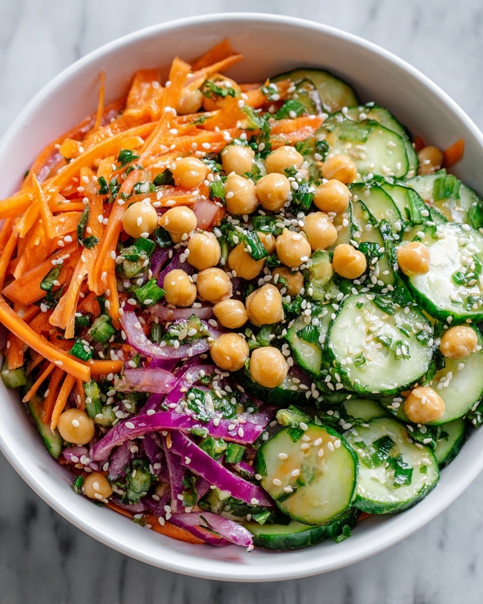 A close-up view of a fresh salad in a white bowl with three main layers: the base layer is made of green cucumber slices with dark green edges and pale wet centers, mixed with shredded bright orange carrot strips; the middle layer includes scattered light golden chickpeas that look glossy and soft; the top layer is sprinkled with thin slices of purple red onion and tiny white sesame seeds, all mixed with bits of green cilantro leaves, creating a colorful, textured appearance on a white marbled surface. photo taken with an iphone --ar 4:5 --v 7