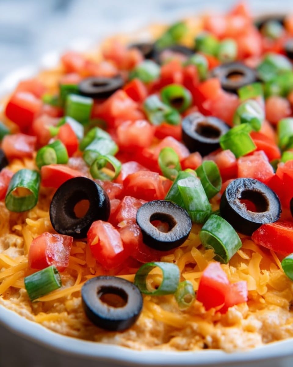 The dish shows a close-up view of a colorful layered dip or salad in a white bowl. The bottom layer is made of shredded orange cheddar cheese, giving a textured and soft base. On top, there are bright, fresh diced red tomatoes scattered unevenly, adding juicy, vibrant red spots. Sliced black olives are spread over the top layer, with their deep black color and shiny, smooth texture standing out against the cheese and tomatoes. Bright green rings of chopped green onions are also placed across the surface, adding fresh color and a crunchy texture contrast. The white marbled background contrasts softly with the colorful ingredients, and the image captures the vibrant colors and textures clearly. photo taken with an iphone --ar 4:5 --v 7
