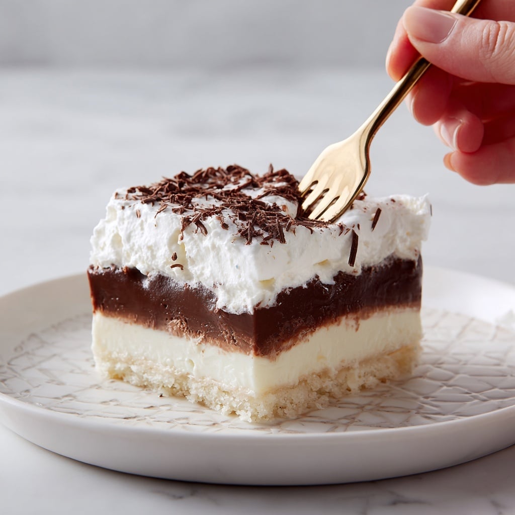 A square slice of layered dessert sits on a white plate with a small portion on a golden fork in front. The dessert has four visible layers: a base layer that looks like a light beige crust, a thin creamy white layer above it, a thicker dark brown chocolate layer next, and a thick fluffy white whipped cream layer on the top. The whipped cream is sprinkled with small chocolate shavings. In the background, a clear glass baking dish holds more of the same layered dessert, placed on a white marbled surface. photo taken with an iphone --ar 4:5 --v 7