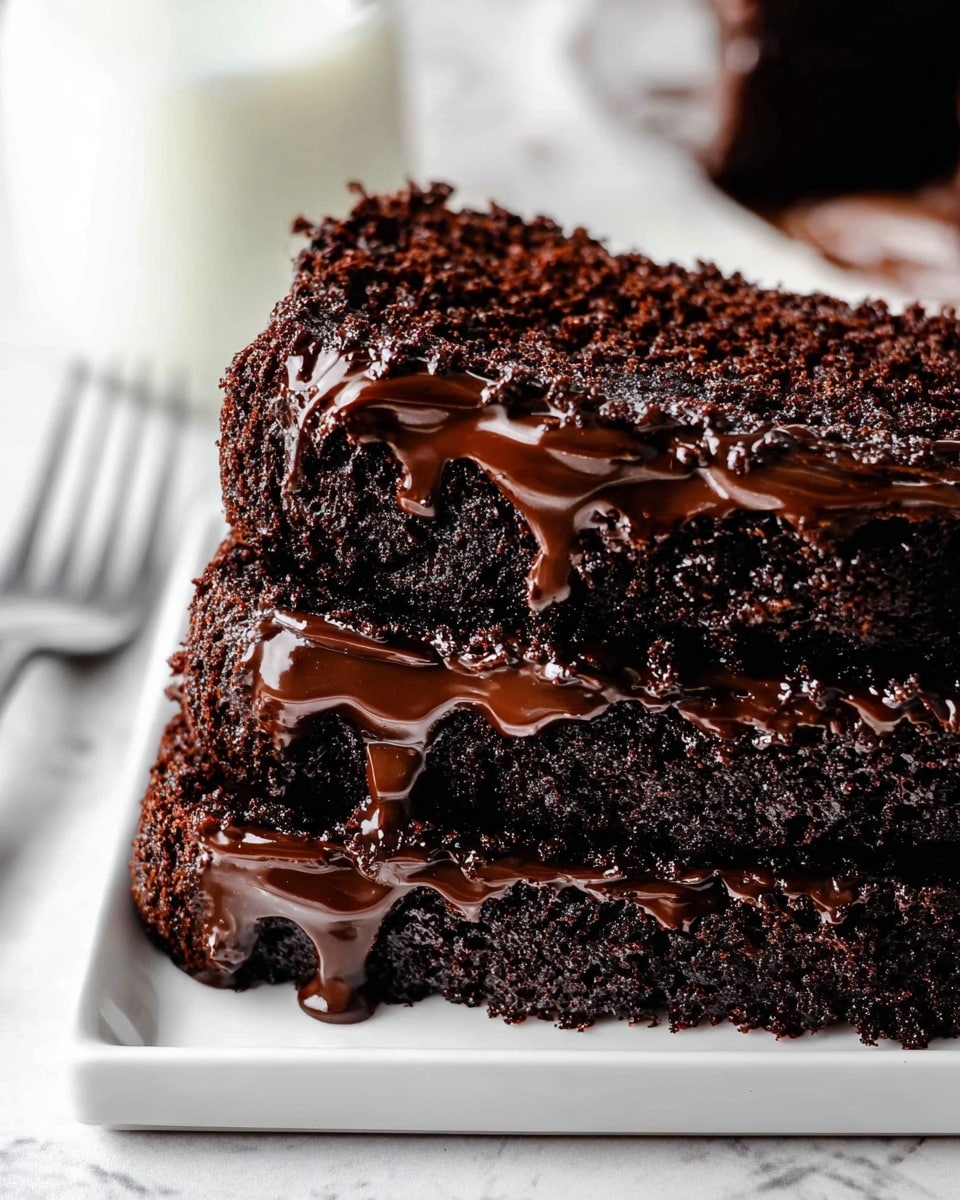 A close-up of a single slice of rich chocolate cake showing two thick layers: a dense, moist dark brown cake layer on the bottom with a soft crumb texture, and a shiny, smooth dark chocolate glaze generously spread on top with slightly wavy folds, creating a glossy surface that catches light. The cake slice sits on a white wire cooling rack with some crumbs scattered around, all set against a blurred white marbled background. photo taken with an iphone --ar 4:5 --v 7