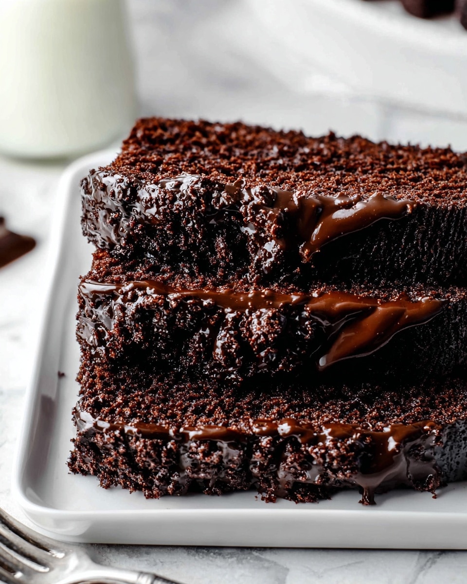 The image shows three thick layers of dark chocolate cake stacked on a white rectangular plate. Each layer has a rich, moist, crumbly texture with glossy, smooth dark chocolate frosting generously spread between and over the cake layers, slightly dripping down the sides. The top cake layer has a rough, crumbly surface with more glossy frosting visible underneath. The scene is set on a white marbled texture background with part of a clear glass of milk and a white fork blurred in the background. photo taken with an iphone --ar 4:5 --v 7